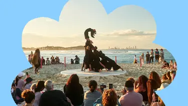 Audience watches a beachside performance featuring a human sculpture at sunset.