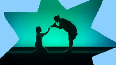 Against a glowing turquoise backdrop, two silhouetted performers face each other, one kneeling and reaching out while the other leans forward in a gesture of connection.