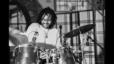 A man with dreadlocks playing drum set.