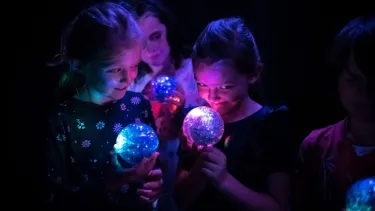 Young children holding glow in the dark circular objects.