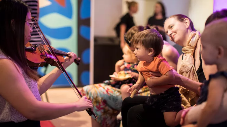 A young boy on his mums lap watching a violinist