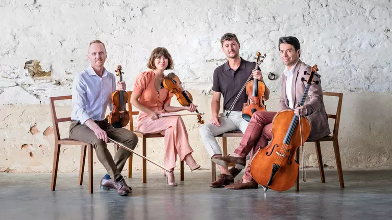 A string quartet holds their instruments looking at the camera