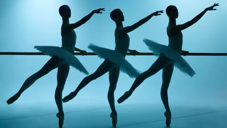 Three ballerinas in silhouette wear tutus with one arm stretched in front of them and one leg pointed behind them.