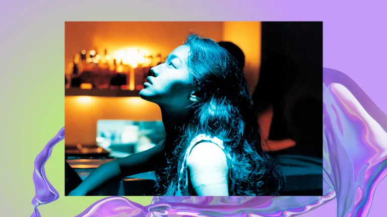 A girl looks up into light. In the background their is a bar shelf full of bottles.