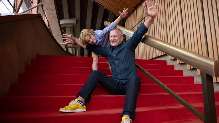 A man and a boy sitting on red stairs with their arms open.