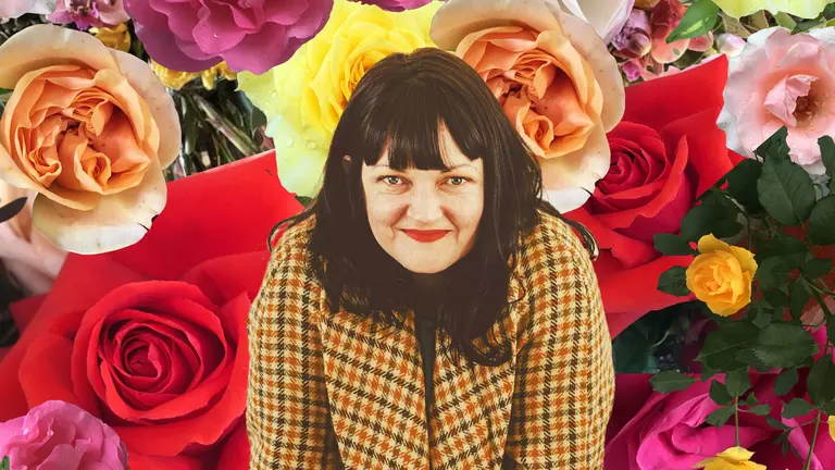 A women smiling infront of a background of flowers