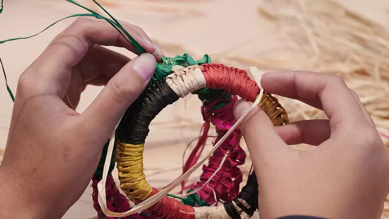 A person weaving a bracelet from coloured jute.