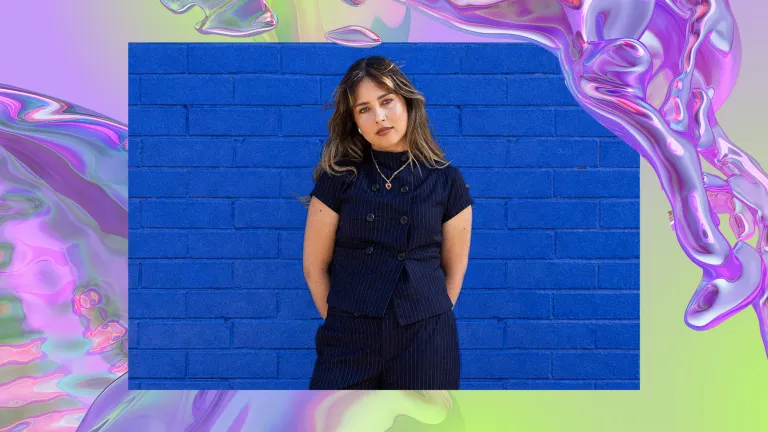 Jem Cassar-Daley stands against a dark blue brick wall.