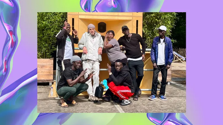 A group of seven people pose casually in front of a wooden structure. The image overlays a backdrop of a purple, iridescent swirl, looking like water.