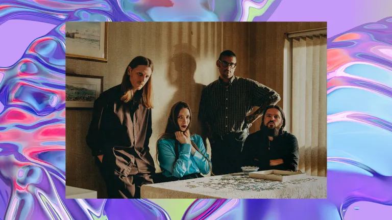 Three men and one woman stand and sit around a kitchen table in a vintage-style room. The background is a purple, iridescent swirl, looking like water.