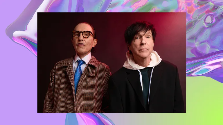 The two members of sparks stand facing the camera in front of a red background.