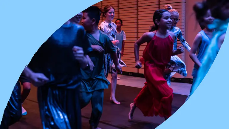 A group of children are running along a black floor with a wooden wall behind them.