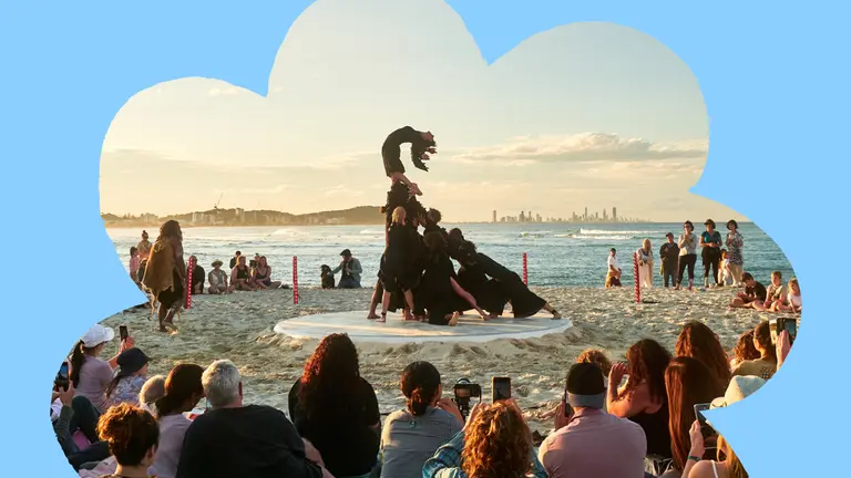 Audience watches a beachside performance featuring a human sculpture at sunset.