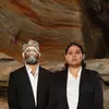 An aboriginal man and women wearing a black suit with traditional face art.