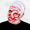 A man in front of a white textured background is wearing a black shirt and a plastic bag over his head. The white bag with red design has eye holes and a mouth hole cut out.