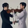 Two Asian men in their 30s face each other, both holding violins. One wears a black suit, the other a white suit.