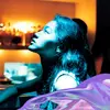 A girl looks up into light. In the background their is a bar shelf full of bottles.