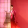 A woman in a pink robe peers out from behind a Japanese screen wall.