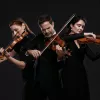 A group of people playing violins against a black background.