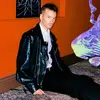 A man sits on a carpeted floor against an orange wall.