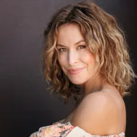 Blonde woman standing side on looking over her left shoulder.