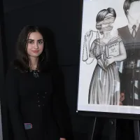 A woman with long brown hair stands next to an image she painted.