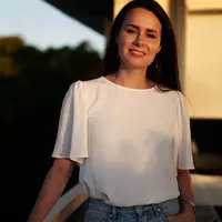 A woman resting her hand on railing wearing a white top and jeans.