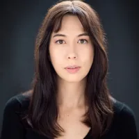 Dark haired woman stands front on in a black top.