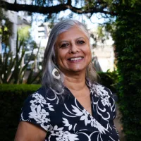 A woman with grey hair smiles at the camera, standing in the Botanic Gardens.