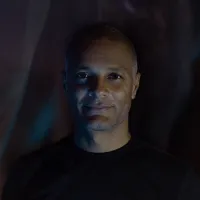 Artist Yann Nguema is looking straight ahead wearing a black t-shirt in front of a dark background.