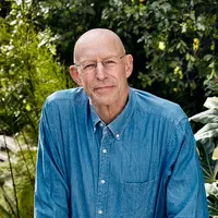 A man wearing a blue denim shirt and spectacle glasses thinking and smiling