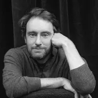 Black and white portrait of Gabriel Sherman. He is wearing a knitted vest and resting his hand against his face as if in thought.