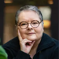 Magda Szubanski wearing glasses with one hand resting on her face
