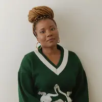 A woman glancing to the camera with gold earrings and a green sweater