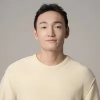 A man in a cream coloured sweatshirt is standing against a white background.