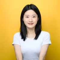 A woman in a white shirt with black hair stands smiling against a yellow backdrop.