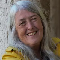 A mature aged women with white hair smiles. She is wearing a yellow jacket.