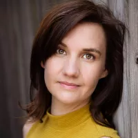 A woman in a yellow dress leaning on a wall.