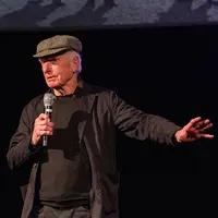 Peter Weir holds a microphone in one hand and uses his other hand for expression.