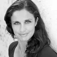 A woman in a dark shirt is looking straight on with her hair over her shoulder.