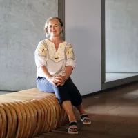 A woman sitting on a wooden bench with her hands on her knees.