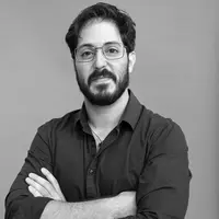 A bearded man with short hair and glasses stands with his arms crossed. He is in a buttoned shirt.