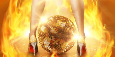 Gold and silver high heels stand on either side of a gold, sparkly disco ball as they are engulfed in hot flames, indicating disco inferno