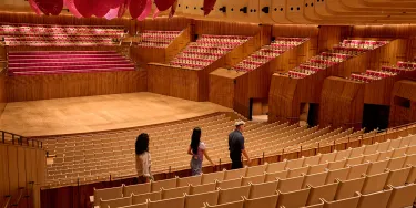 The empty concert hall is seen from the back with two people being walked through on a tour.