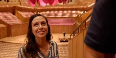 A woman stands smiling in the upper section of the concert hall following a tour guide.