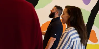 A tour guide and woman in a striped shirt stand in front of the colourfully painted walls of the utzon room.