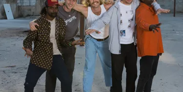 The five members of King Stingray stand with their arms around each other in an abandoned lot.