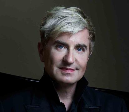 A person with short, blond hair and light skin is wearing a black jacket.