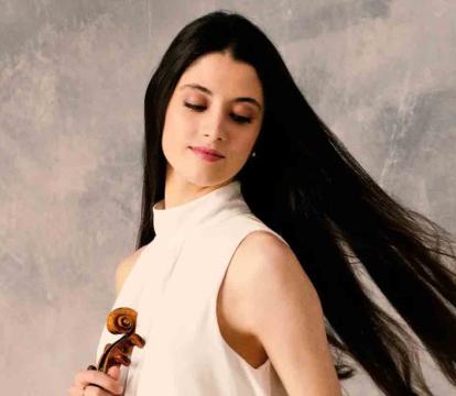 A woman with long, dark hair wearing a sleeveless white top holds a violin.