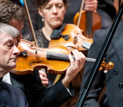 Stephen Hough wears a pinstripe shirt as his eyes are closed playing the piano in front of the violin section of an orchestra